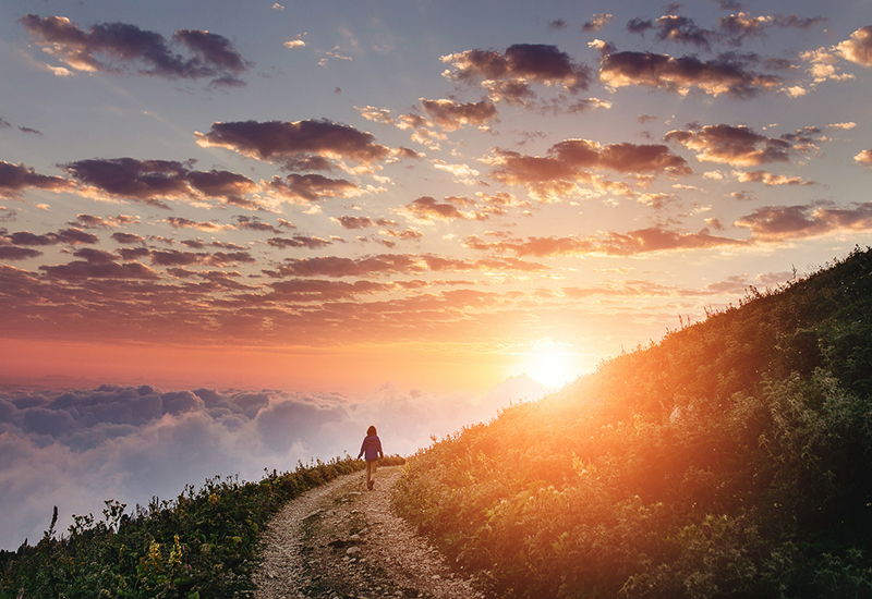 Woman on trail admiring the sunset with clouds and fog.